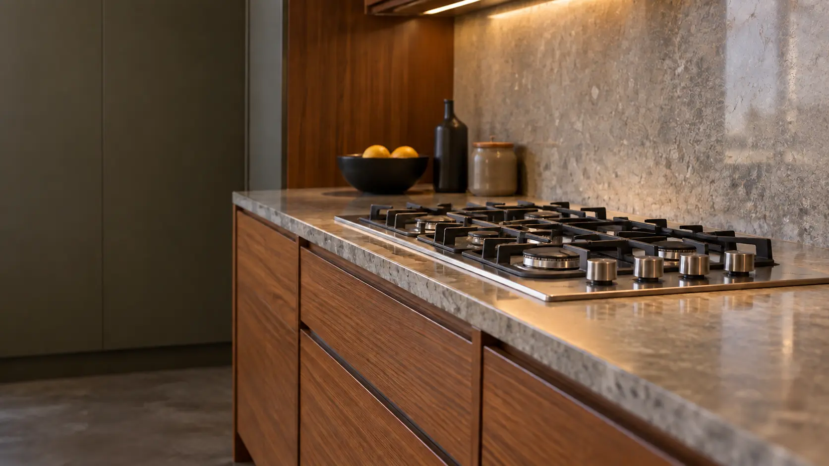 A mid-century house kitchen with a gas cooktop in teak cabinets, seen low along the counter, the cooktop surface catching the light.