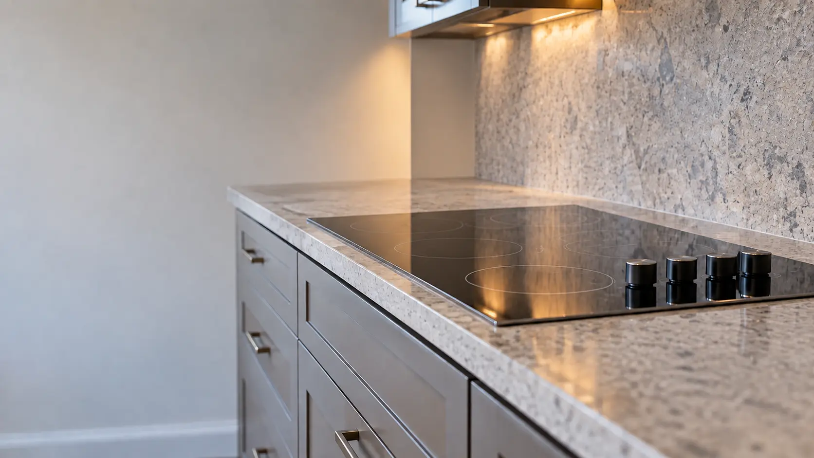A split-level kitchen with a glass cooktop over drawers, seen low along the counter, the cooktop surface catching the light.