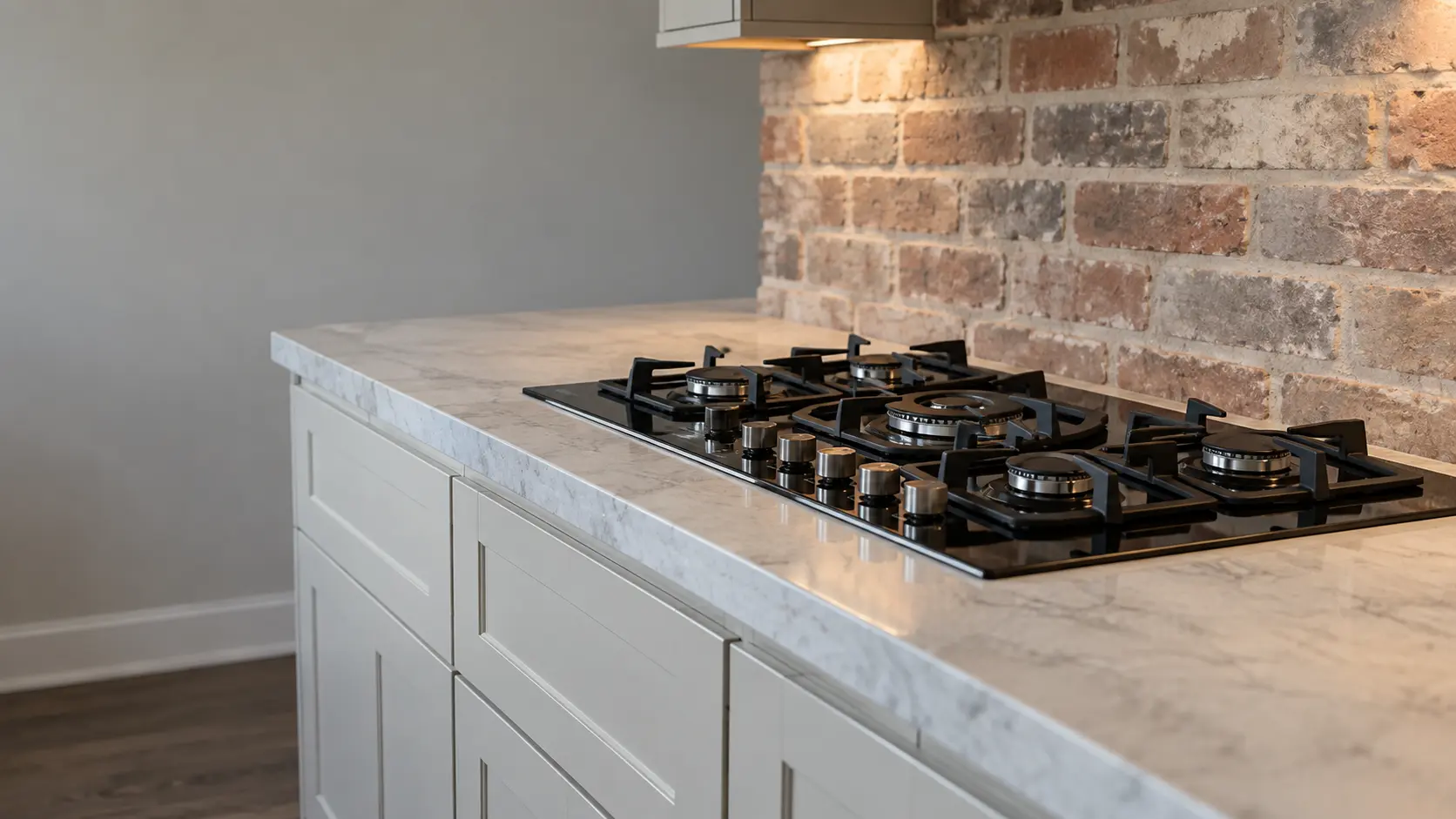 A farmhouse kitchen with a gas cooktop beside a brick wall, seen low along the counter, the cooktop surface catching the light.