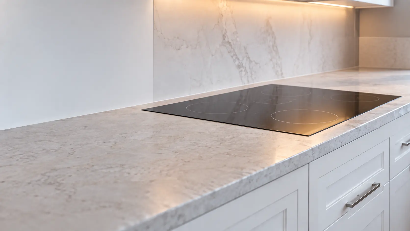 A shingled Long Island house kitchen with an induction cooktop in white cabinets, seen low along the counter, the cooktop surface catching the light.