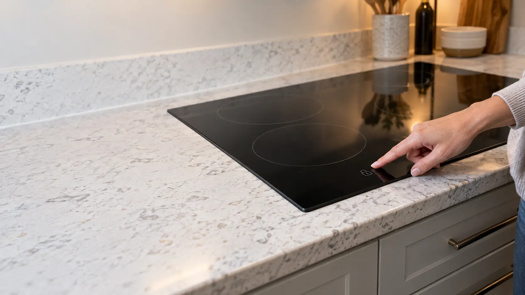 A finger touching the lock key on a black glass cooktop's control strip, the display blank.