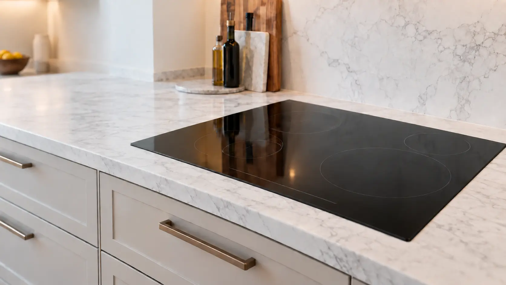 A frameless black induction cooktop with a touch slider along its front edge sits flush in a white marble countertop above closed drawers in a US home kitchen.