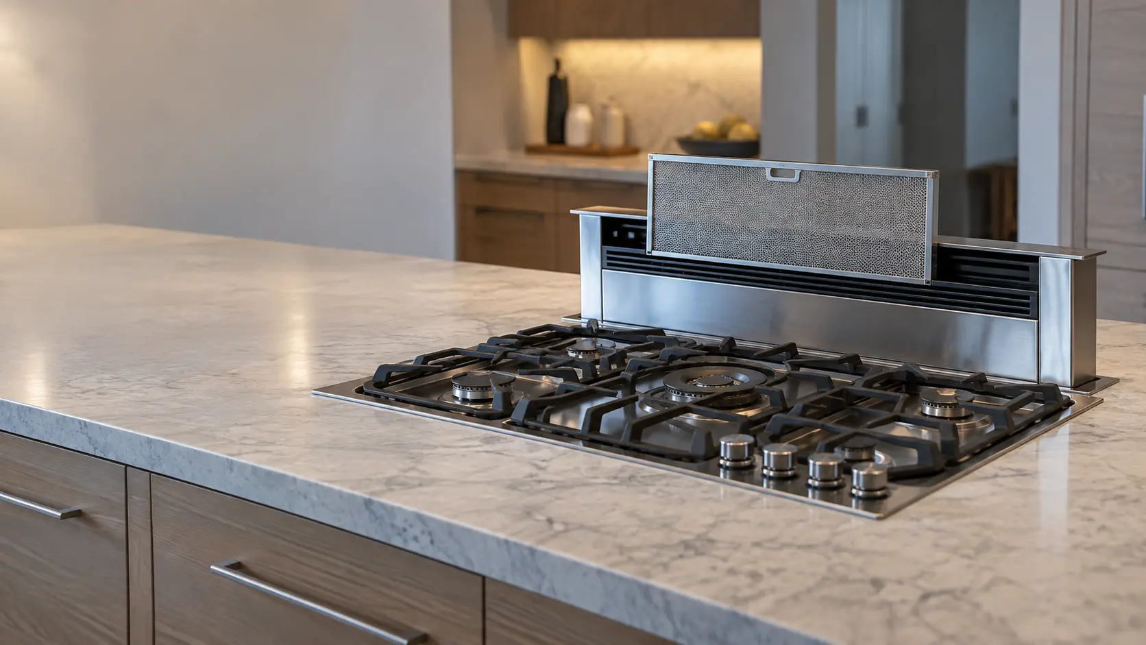 A downdraft vent risen from behind a gas cooktop in a kitchen island, its grille open and a steel mesh filter lifted halfway out.