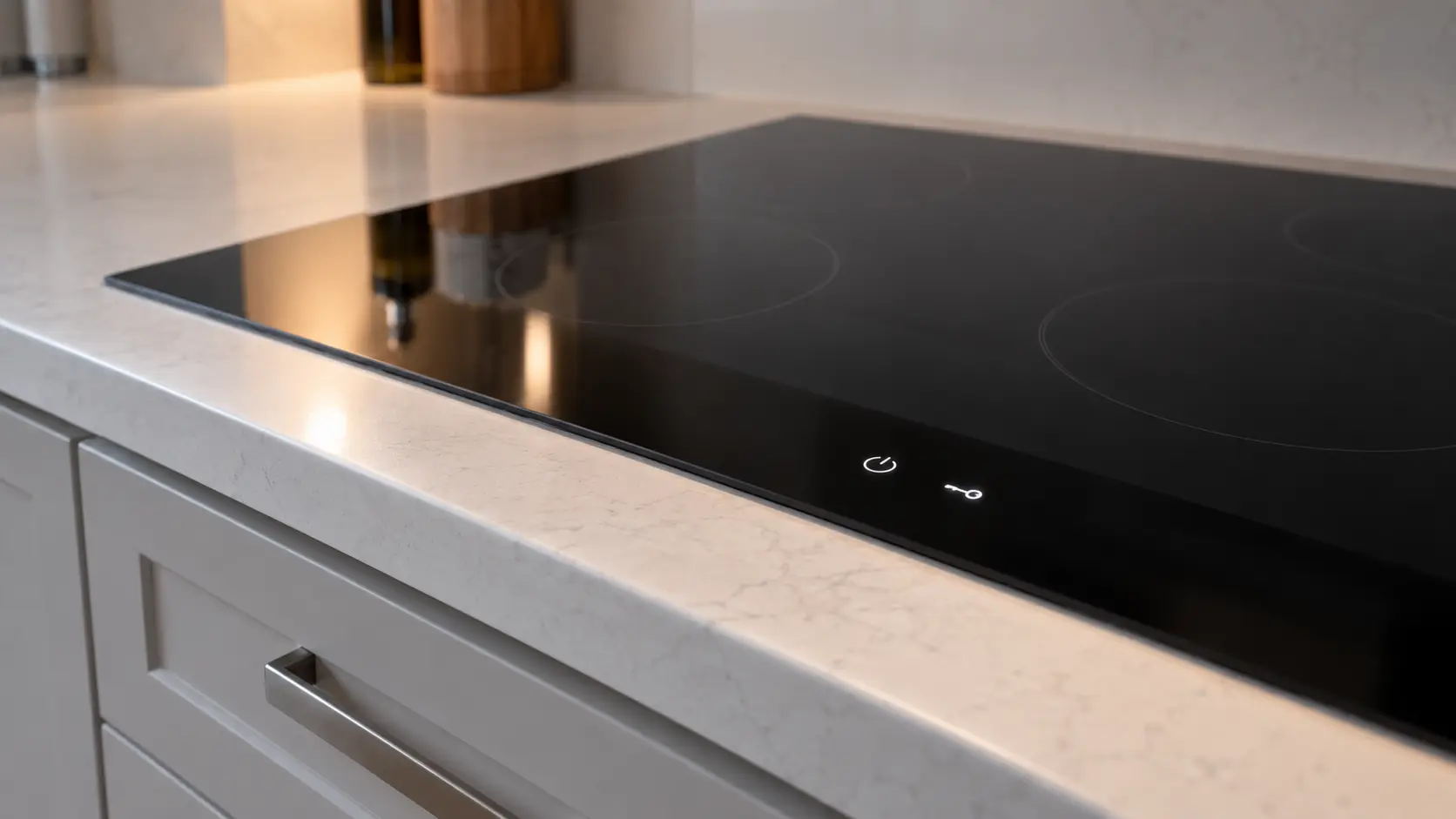 The touch strip along the front of a black glass cooktop set into a white counter, a small key symbol lit beside the power button and every zone dark.