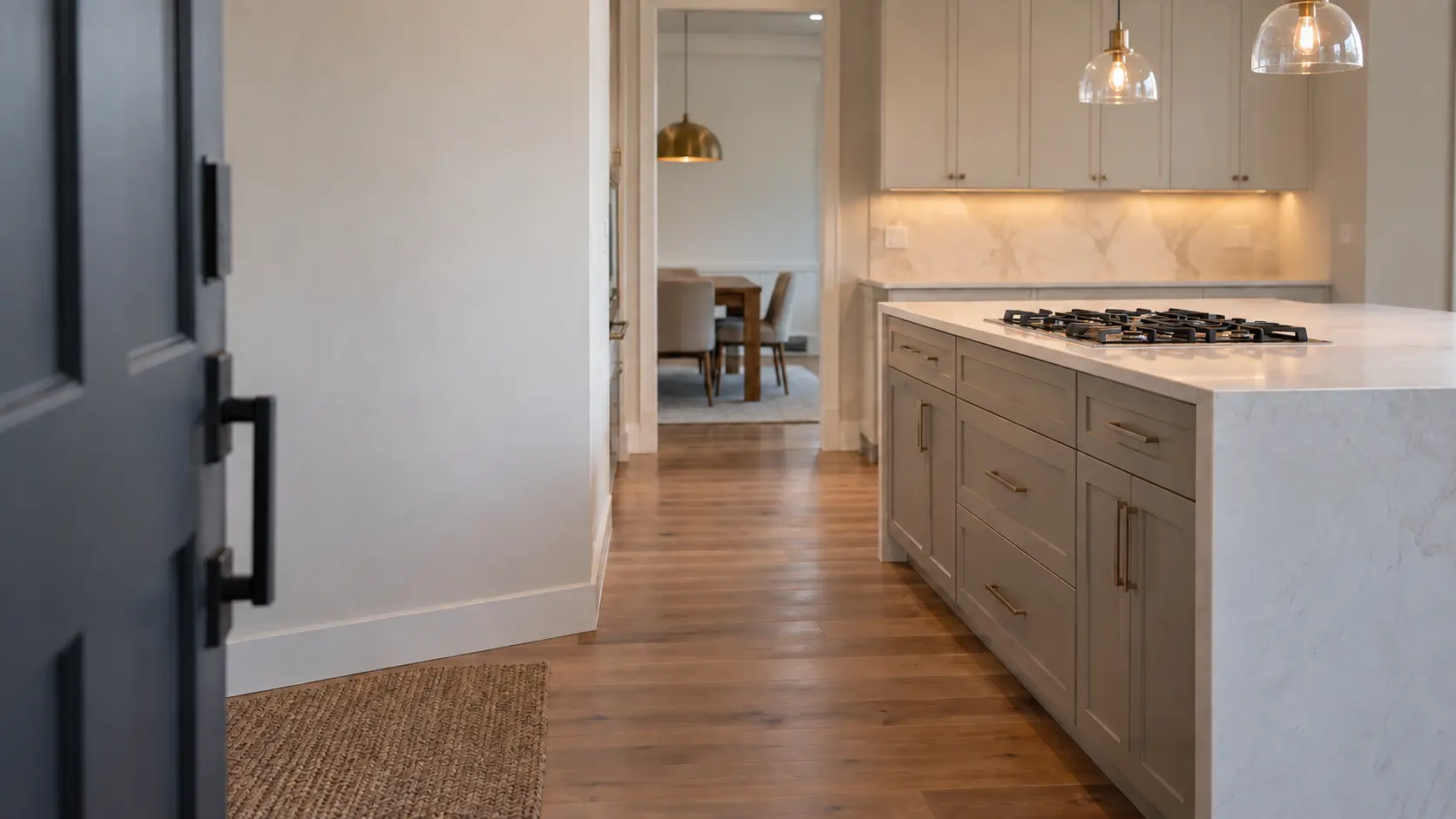 A house's front door standing open, a kitchen island with a gas cooktop visible down the hallway.