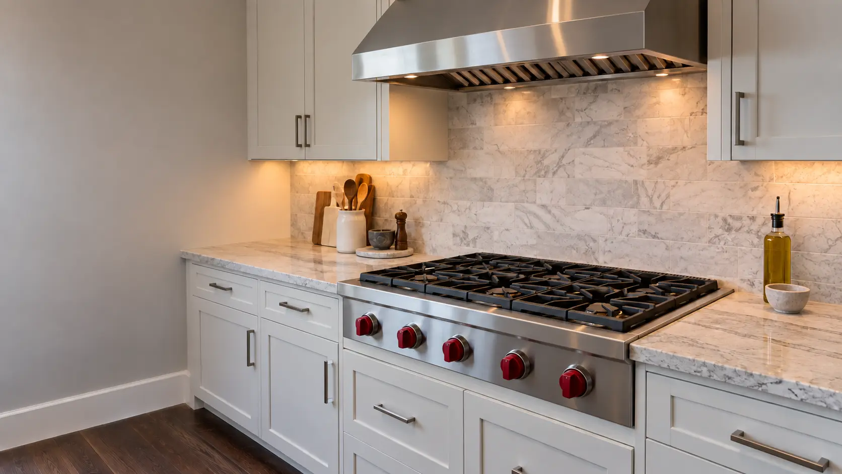 A 36-inch stainless pro-style gas rangetop with red knobs on its front face and cast-iron grates, set into a notched stone counter over a base cabinet of drawers in a US home kitchen, a stainless overhead extractor above it.