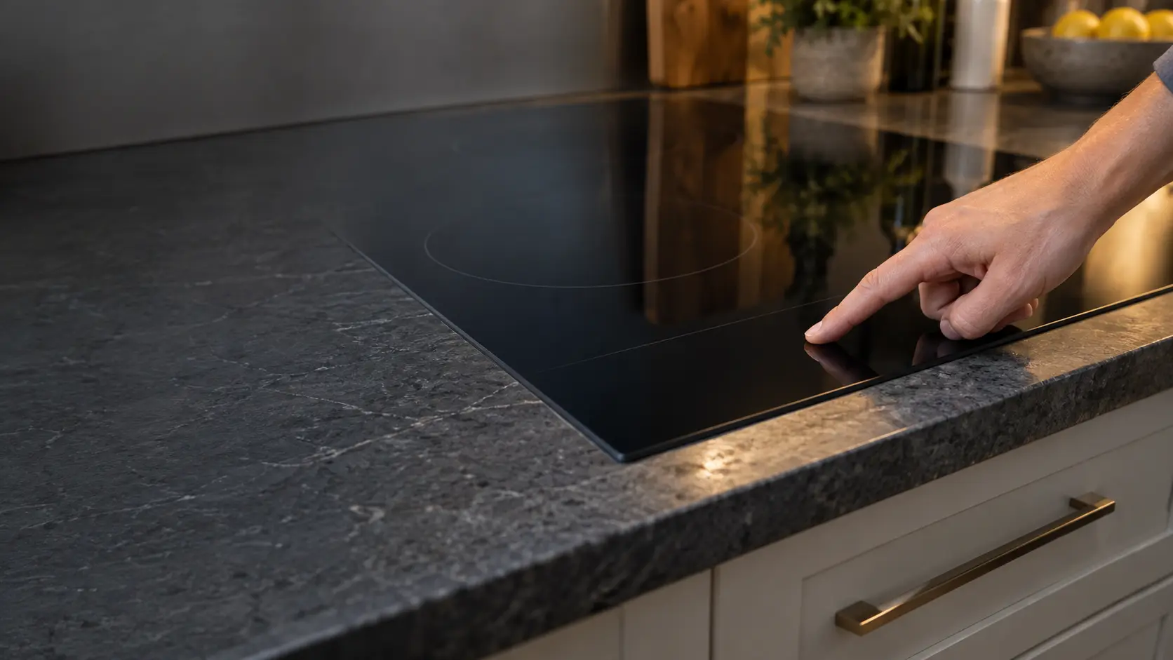 Close on a fingertip resting on the lock key of a glass cooktop's touch strip, the display blank.