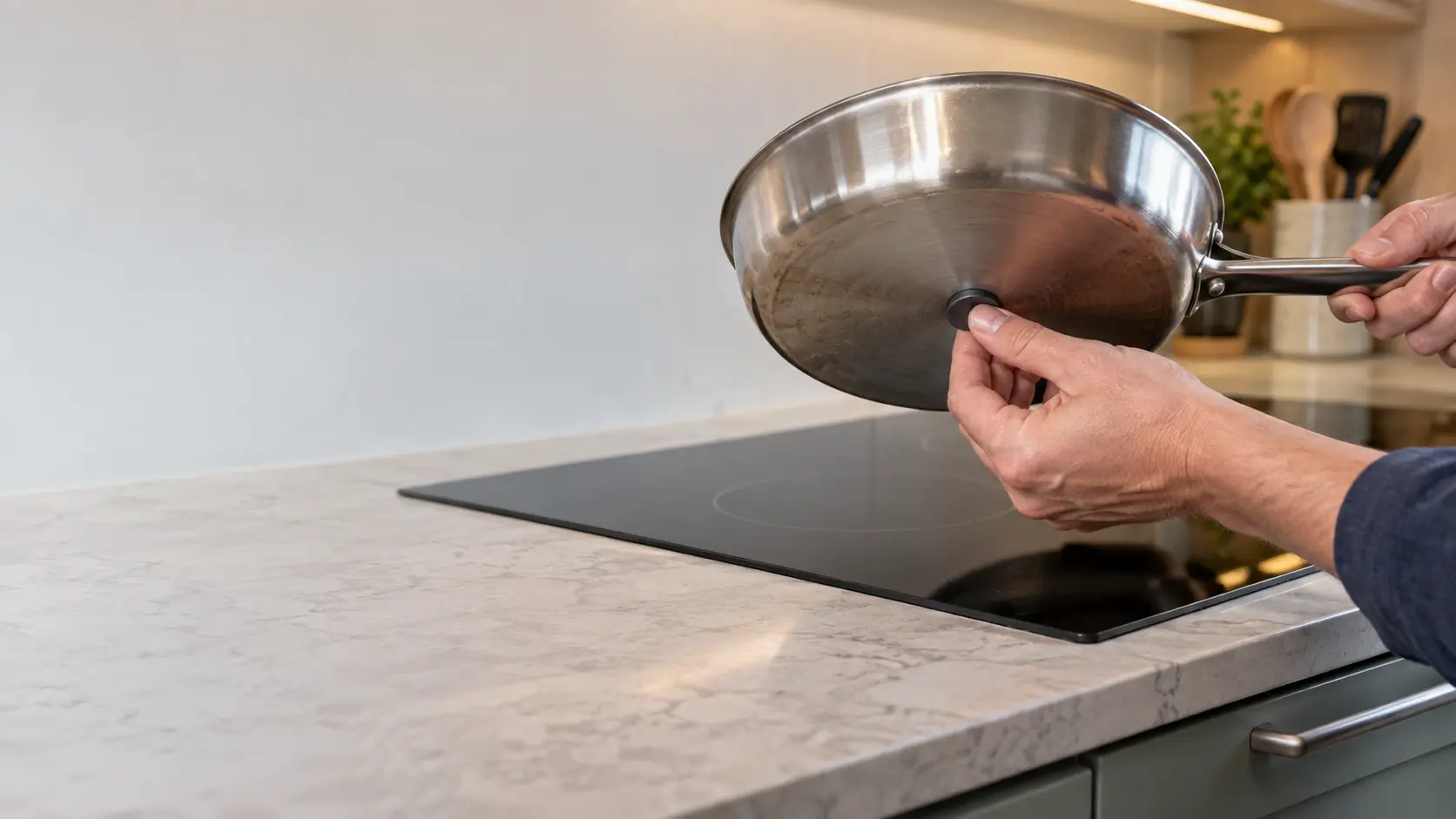 Close on a fridge magnet held to the base of a steel pan above a black induction cooktop.